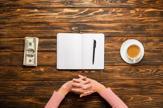 cropped view of businesswoman stretching hands while preparing to write new year resolution near dollar banknotes and coffee cup on wooden desk