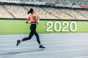 Obraz premium young african american sportswoman running on stadium near 2020 lettering