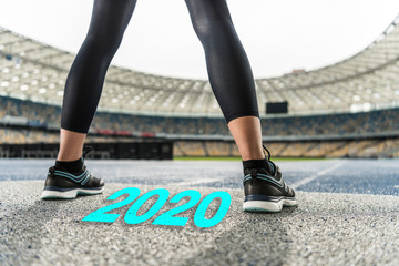 cropped view of sportswoman standing on running track near 2020 lettering