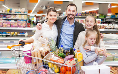 Man with wife and children holding purchases in supermarket
