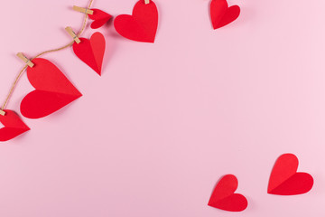 The concept of the preparation for Valentine's Day. Red hearts are held by clothespins on a jute rope, on pink background. Copy space.