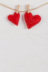 The concept of the preparation for Valentine's Day. Red hearts are held by clothespins on a jute rope, on a white wooden background. Copy space.