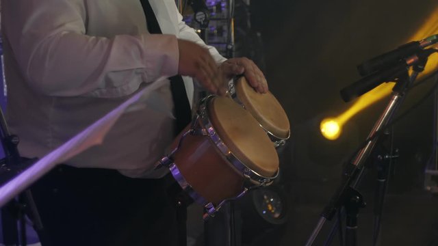 Drummer in a white classic shirt and black tie plays a Bongo drums on stage