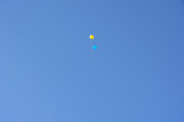 Two balloons of blue and yellow are flying high in the sky. Two baloons against the background of the blue sky.
