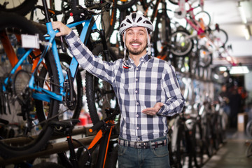 Plakat attractive man in helmet chooses for himself sports bike in bicycle shop