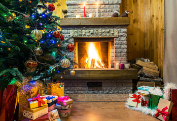 Cozy burning fireplace. Christmas tree decorated toys and christmas lights, gift boxes and candles on floor.