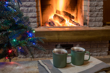 Christmas evening. Cozy fireplace and cups of tea on wooden table.