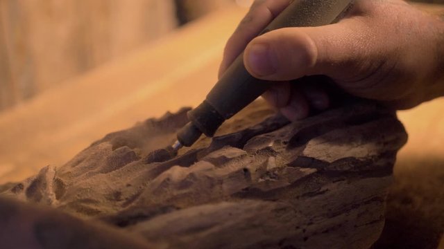 Male using tool equipment holding carving art slow motion medium on wooden table in rustic shed carefully focused detail work