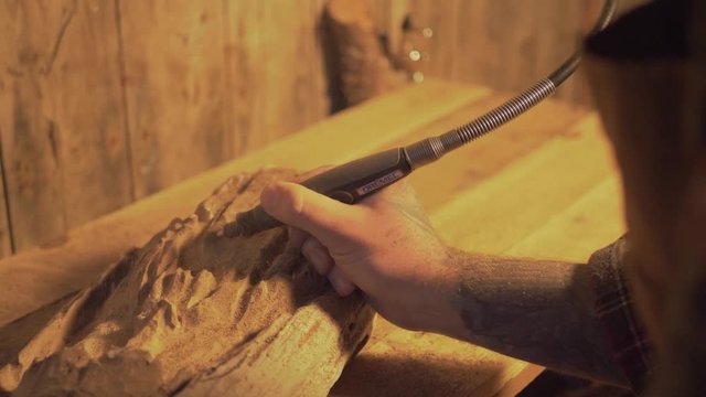 Male using tool equipment holding carving art slow motion medium on wooden table in rustic shed turning wood over the shoulder