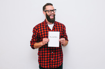 Portrait of handsome hipster guy with beard pointing finger at blank notebook with space for text isolated over white background