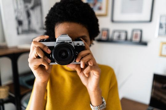Young woman taking picture with vintage camera at home