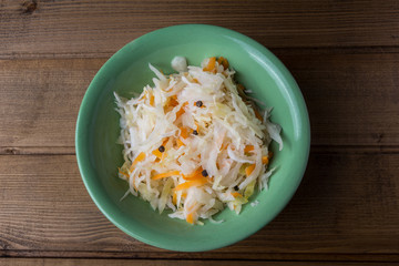 sauerkraut with carrots in a plate on a wooden background, top view, close up