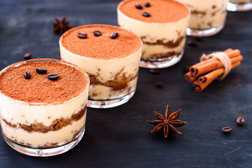 classical tiramisu dessert in a glass sprinkled with cocoa and decorated with coffee beans on a dark background, luxury dessert