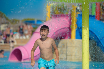 Active Caucasian boy spending his summer holidays in water park, he splashing in pool against...