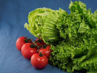 Green salad, Chinese cabbage and fresh tomatoes on a blue textile background, close-up. Selective focus on lettuce leaves. Horizontal orientation. Fresh green vegetables.