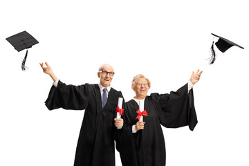 Elderly man and woman graduates throwing hats and holding diplomas