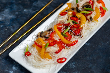 Oriental rice noodles Udon with sweet pepper, mushrooms. On a dark background.