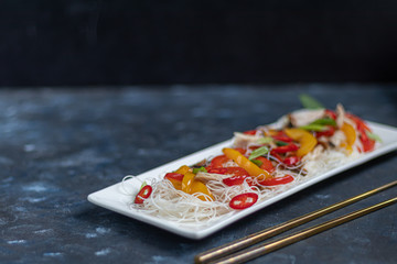 Oriental rice noodles Udon with sweet pepper, mushrooms. On a dark background.