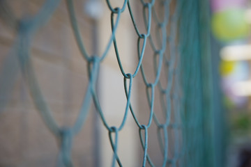 Fototapeta premium Detail of a fence with abstract background.close up steel fence agains green field : narrow depth of field .Grille and background blurred . Blue metal fence net as background.
