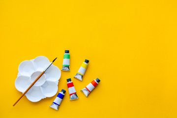 top view of brushes, color tubes and palette on yellow background, copy space, flat lay, paintings...