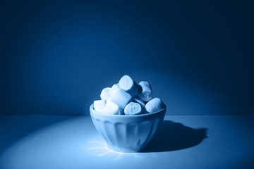 Bowl of giant marshmallows on solid backdrop with harsh shadows, toned in classic blue