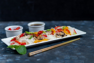 Oriental rice noodles Udon with sweet pepper, mushrooms. On a dark background.