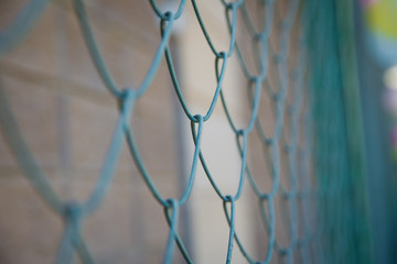 Detail of a fence with abstract background.close up steel fence agains green field : narrow depth of field .Grille and background blurred . Blue metal fence net as background.