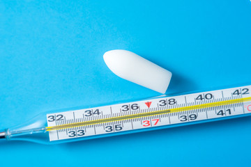 White suppository for anal or vaginal use on blue background and a thermometer with temperature of...