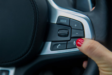 the finger of a female hand push the microphone button on the steering wheel, the equipment of a modern car. close-up, soft focus, blur background