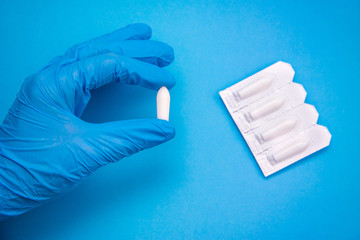 White suppository for anal or vaginal use in hand of a doctor wearing gloves on a blue background....