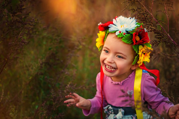 Beautiful smiling 3 years old girl in pink dress and traditional ukrainian wreath on head in sunset time. Smile on face small girl from Ukraine. traditional clothes and festivities