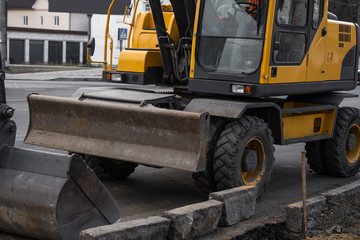 Yellow excavator standing on a road on construction site of the road on a street. Heavy industry. Construction of a road.