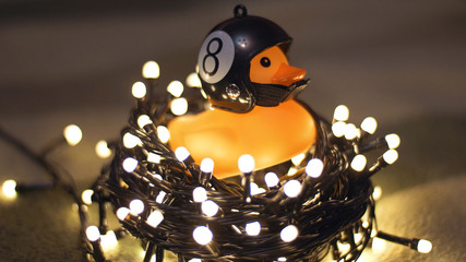 Close-up shot of rubber duck in hand made motorcycle helmet on background of christmas garland 