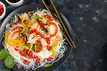 Oriental rice noodles Udon with sweet pepper, mushrooms. On a dark background.