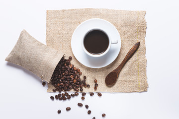 white coffee cup , coffee beans spilled out of the bag, wooden spoon with coffe on white background. Top view.