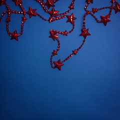 Red Christmas beads with stars on a blue background. Color of the year 2020, Classic Blue