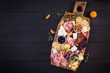 Antipasto platter with ham, prosciutto, salami, cheese,  crackers and olives on a wooden background.  Christmas table. Top view, overhead