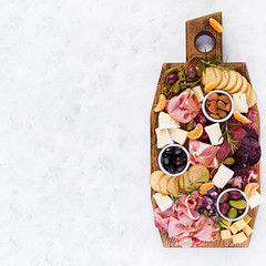 Antipasto platter with ham, prosciutto, salami, cheese,  crackers and olives on a light background.  Christmas table. Top view, overhead