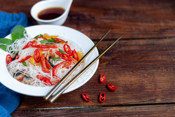 Oriental rice noodles Udon with sweet pepper, mushrooms. On a wooden background.