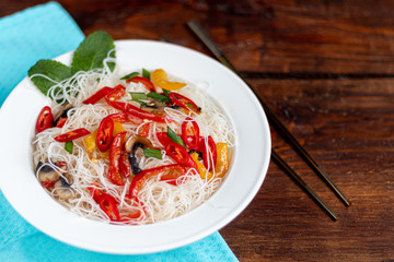 Oriental rice noodles Udon with sweet pepper, mushrooms. On a wooden background.