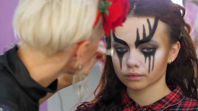 Easy Halloween Makeup. Girl in a beauty salon. Applying a stylistic pattern on the face of the model. The work of a master stylist.