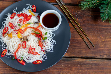 Oriental rice noodles Udon with sweet pepper, mushrooms. On a wooden background.