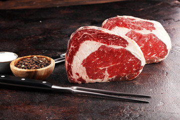 Raw fresh meat Ribeye Steak, seasoning and meat fork on rustic background