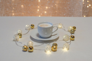 Obraz na płótnie Canvas Weihnachtlicher Cappuccino vor Bokeh mit goldenen Mini Christbaumkugeln und leuchtender Lichterkette Querformat