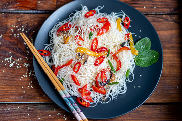 Oriental rice noodles Udon with sweet pepper, mushrooms. On a wooden background.