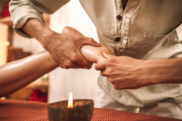 Naklejka premium Alternative Medicine. Therapist healing woman doing ayurvedic massage acupressure with aroma candle rubbing foot close-up