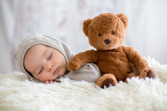 Naklejki Sweet baby boy in bear overall, sleeping in bed with teddy bear