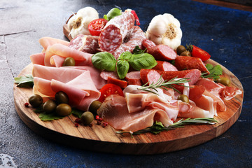 Food tray with delicious salami, pieces of sliced prosciutto crudo, sausage and basil. Meat platter