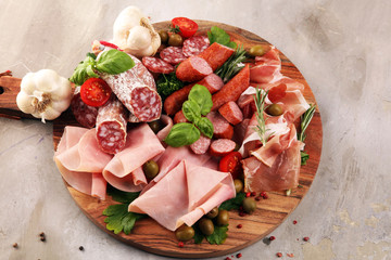 Food tray with delicious salami, pieces of sliced prosciutto crudo, sausage and basil. Meat platter