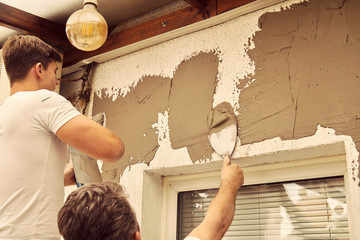 Construction workers plaster a wall.
